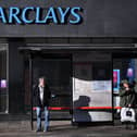 Commuters wait at a bus stop outside a branch of Barclays in London.