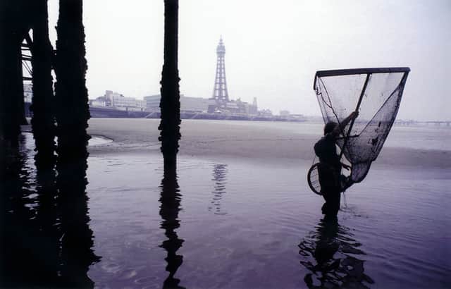 A shrimp fisherman wades out into seawater under Blackpool pier in the early morning, holding his fishing net as he looks for shrimp in the water, 1990