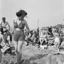 A young woman in a knitted bathing costume stands on the beach in the midst of the crowds of holidaymakers, Blackpool, c1946-c1955. Blackpool Tower is visible in the background. (Photo by English Heritage/Heritage Images/Getty Images)