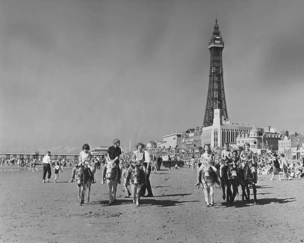 28th August 1965:  Holidaymakers riding donkeys on a busy beach in  Blackpool, Lancashire with Blackpool Tower in the background