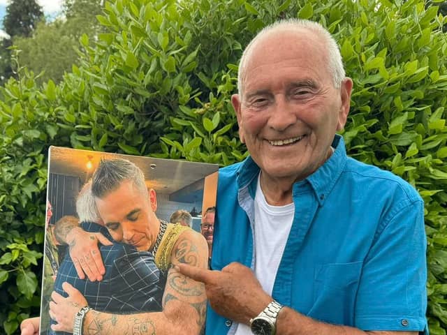Tommy Cannon holds a photo of himself hugging Robbie Williams.
