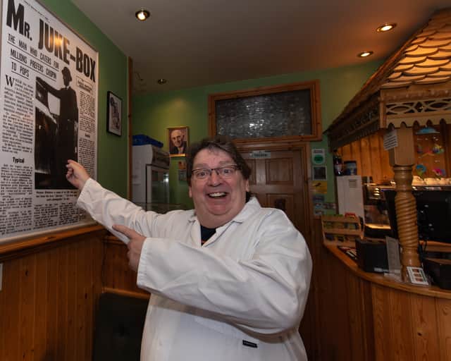 Karl Dawson points at an old newspaper article about Ditchburn Jukeboxes, in his St Anne's cafe. Photo by Lucinda Herbert.