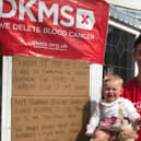 Alex and daughter, nine month old Pearl Lily, pictured  by  a poster and banner promoting the triathlon from home