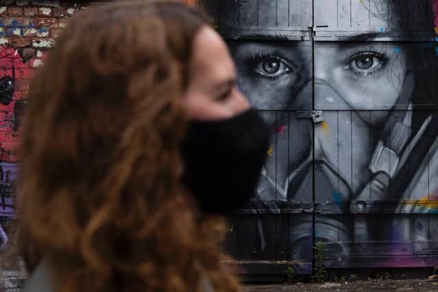 A woman wearing a face mask walks past a mural of a woman wearing a mask