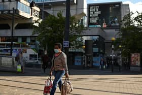 A woman wearing a face mask or covering due to the COVID-19 pandemic, walks near a sign urging people to 'get tested' to see if they have coronavirus, in Manchester (Photo by OLI SCARFF/AFP via Getty Images)