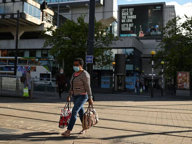 A woman wearing a face mask or covering due to the COVID-19 pandemic, walks near a sign urging people to 'get tested' to see if they have coronavirus, in Manchester (Photo by OLI SCARFF/AFP via Getty Images)