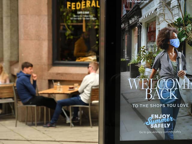 Customers sit outside a bar, near a sign promoting post-COVID-19 lockdown shopping, in Manchester