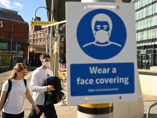 Pedestrians walk past a sign urging people to 'wear a face covering' due to the COVID-19 pandemic, in Manchester (Photo by OLI SCARFF/AFP via Getty Images)