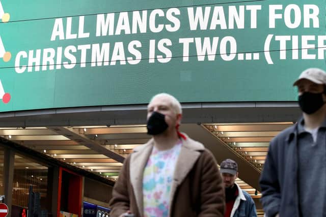 People wearing face masks walk past a sign on Market Street, Manchester