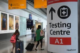 Passengers push their luggage past signage displaying the way to a Covid-19 test centre, in Terminal 5 at Heathrow airport