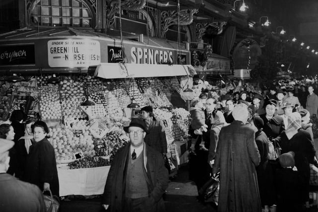 Some of these shoppers look to be aware of the camera as they pass Spencer's fruit stall.