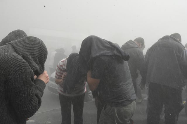Spectators caught in the dust cloud pull coats over their heads to shield themselves from it
