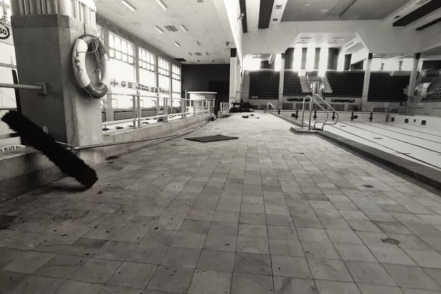 A pool brush cast aside with mats and debris littering the pool area