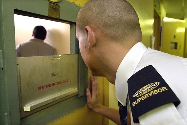 A Civilian Detention Officer at work, looking into one of the cells at Blackpool Police Station, 2003