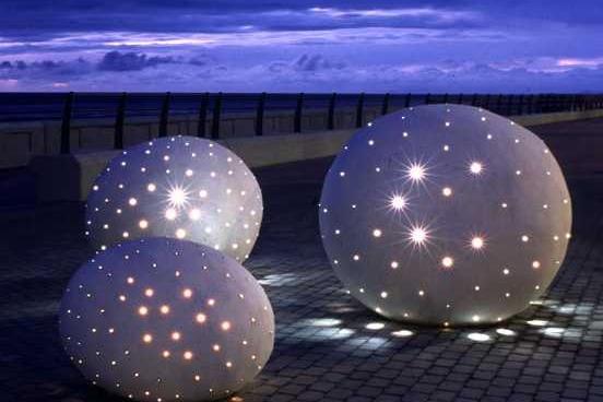 Glam Rocks on Blackpool Promenade shining at night. They consist of three giant sea smoothed beach pebbles made from white concrete and studded with fibre-optic lights which change colour and sparkle. It was considered last year that they needed maintenance work but for now they are still in place