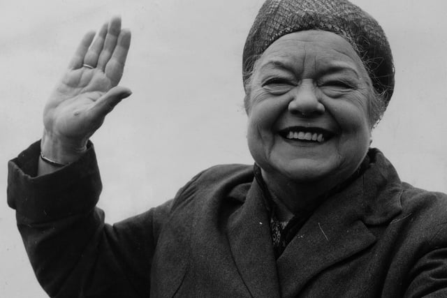 Wearing her famous hairnet, actress Violet Carson in her costume as Ena Sharples in Coronation Street, gives a cheery greeting