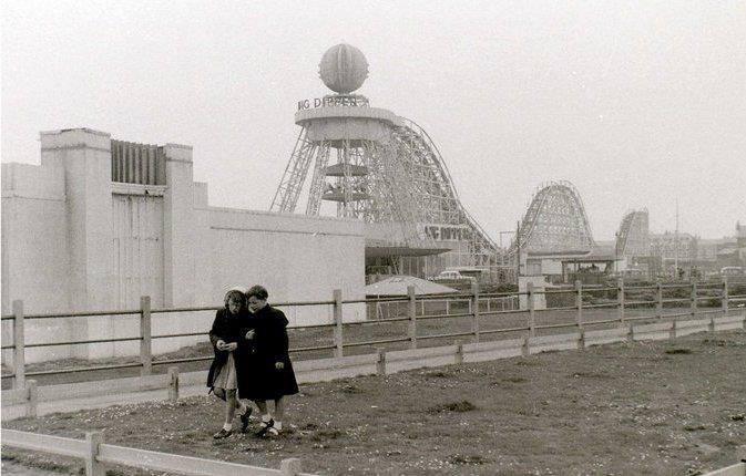 Two young girls stroll across a swathe of undeveloped land at the Pleasure Beach against the backdrop of the Big Dipper. The roller coaster was built by William Strickler at a cost of just £25,000