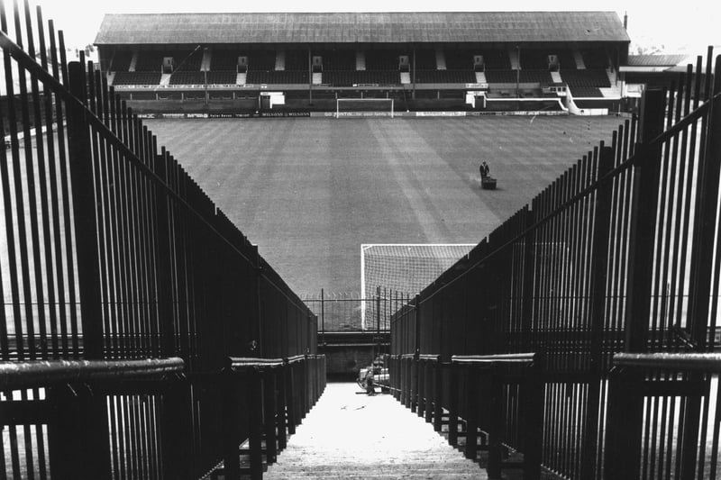 The view from the Kop at Blackpool Football Club Ground , Bloomfield Road showing the railings installed to keep rival fans apart and a lone groundsman hard at work mowing the pitch, 1975