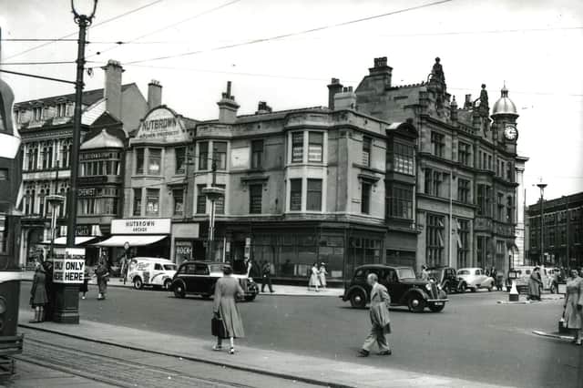 This was the Promenade and Talbot Square in the mid 1950s. From the left, businesses include the EH Booth store and cafe above, Williams and Son Chemist, the Nutbrown Arcade selling Nutbrown Kitchen Equipment and a small shop advertising Blackpool rock. On the corner is an empty shop with the Royal Liver Assurance office and the Entertainments and Accommodation Ltd above.  Round the corner into Talbot Square is the Midland Bank and the corner of the white facade of the Williams Deacon's Bank . Across the Square there is a gimpse of Yates's Wine Lodge. The white van has advertisements for comedian Albert Modley and his " all star cast".