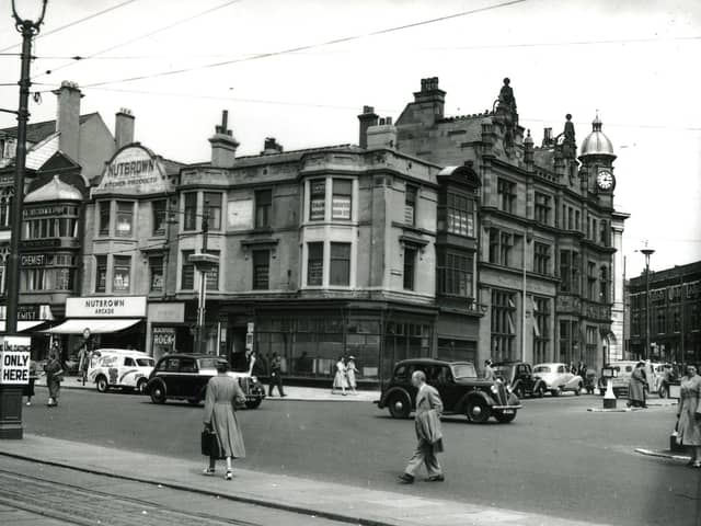 This was the Promenade and Talbot Square in the mid 1950s. From the left, businesses include the EH Booth store and cafe above, Williams and Son Chemist, the Nutbrown Arcade selling Nutbrown Kitchen Equipment and a small shop advertising Blackpool rock. On the corner is an empty shop with the Royal Liver Assurance office and the Entertainments and Accommodation Ltd above.  Round the corner into Talbot Square is the Midland Bank and the corner of the white facade of the Williams Deacon's Bank . Across the Square there is a gimpse of Yates's Wine Lodge. The white van has advertisements for comedian Albert Modley and his " all star cast".