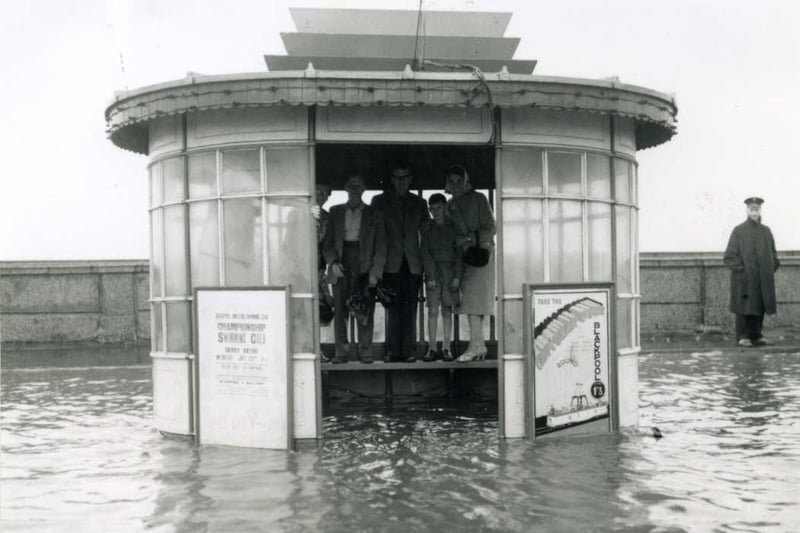 Standing on the seat to keep their feet dry while waiting for a tram in a floooded tram shelter