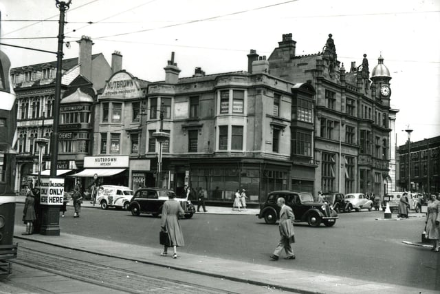 The Promenade and Talbot Square in the mid 1950s. From the left, businesses include the EH Booth store and cafe above, Williams and Son Chemist, the Nutbrown Arcade selling Nutbrown Kitchen Equipment and a small shop advertising Blackpool rock. On the corner is an empty shop with the Royal Liver Assurance office and the Entertainments and Accommodation Ltd above