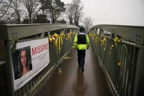 A police officer walks past a missing person appeal poster for Nicola Bulley and yellow ribbons and messages of hope tied to a bridge over the River Wyre in St Michael's