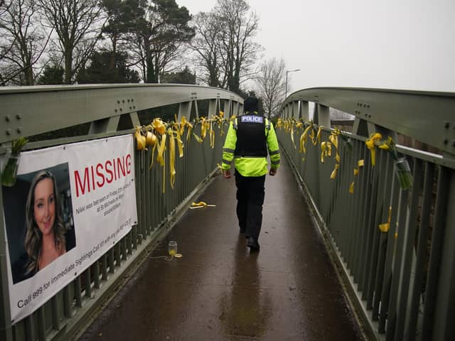A police officer walks past a missing person appeal poster for Nicola Bulley and yellow ribbons and messages of hope tied to a bridge over the River Wyre in St Michael's
