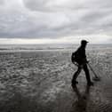 A man uses a metal detector on beach