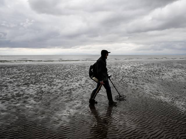 A man uses a metal detector on beach