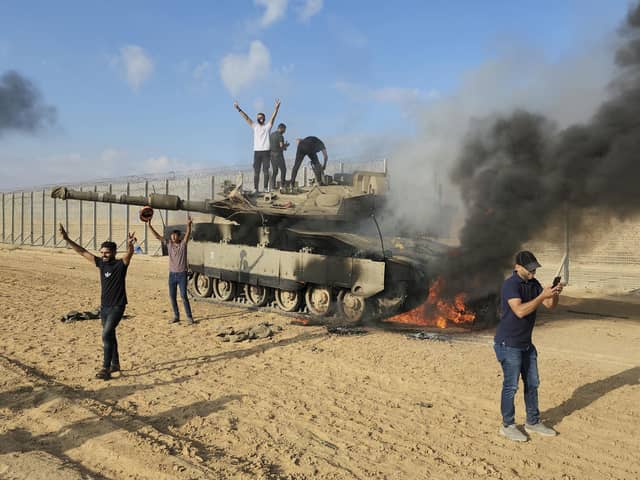 Palestinians celebrate by a destroyed Israeli tank at the Gaza Strip fence east of Khan Younis Saturday, Oct. 7, 2023. The militant Hamas rulers of the Gaza Strip carried out an unprecedented, multi-front attack on Israel at daybreak Saturday, firing thousands of rockets as dozens of Hamas fighters infiltrated the heavily fortified border in several locations by air, land, and sea and catching the country off-guard on a major holiday (AP Photo/Hassan Eslaiah)