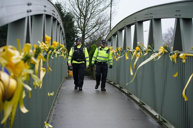 Officers walk past yellow ribbons and messages of hope tied to a bridge for over the River Wyre. Photo: Peter Byrne/PA Wire