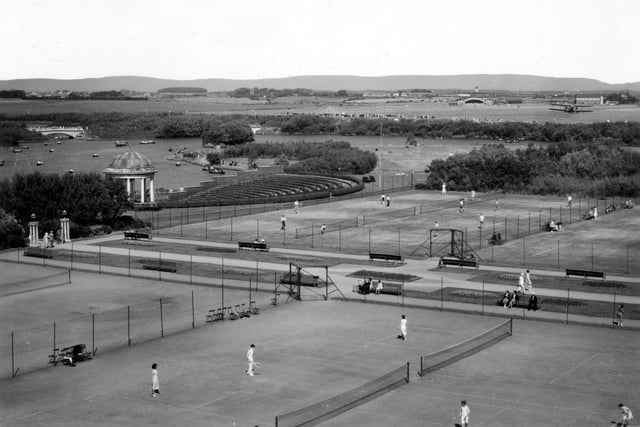 Playing on Stanley Park Tennis Courts has always been a popular summer pastime. Stanley Park Airport can be seen in the background and a plane in the right corner just above the trees, 1930s