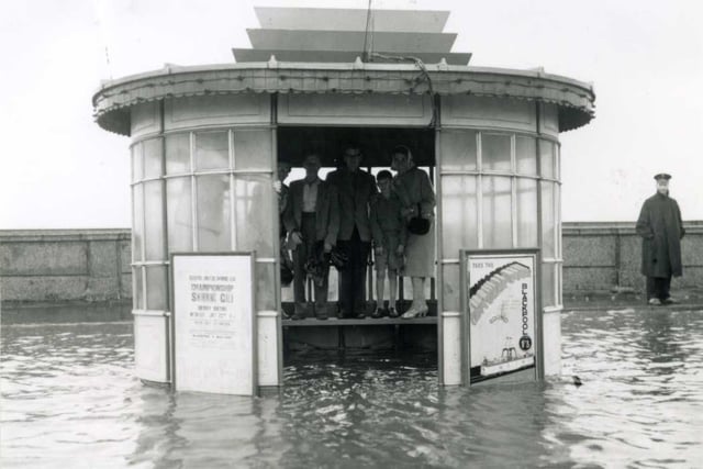 Standing on the seat to keep their feet dry while waiting for a tram in a flooded tram shelter in the 1950s