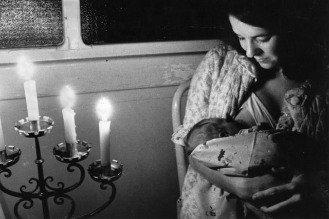 A woman breast feeding her newborn baby by candlelight during a blackout in 1970