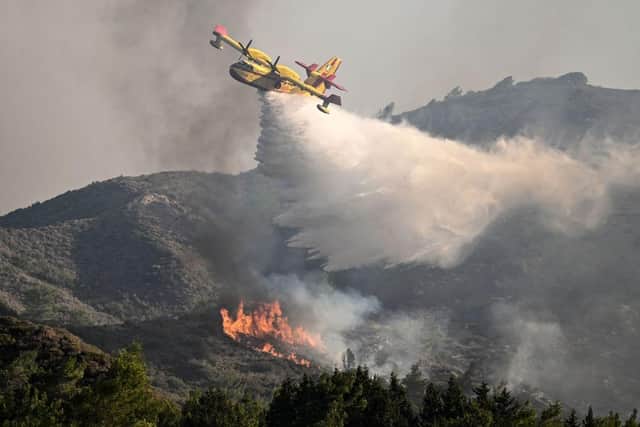 A fire fighting aircraft drops water over a wildfire close to village of Vati in the southern part of the Greek island of Rhodes (Photo by SPYROS BAKALIS/AFP via Getty Images)