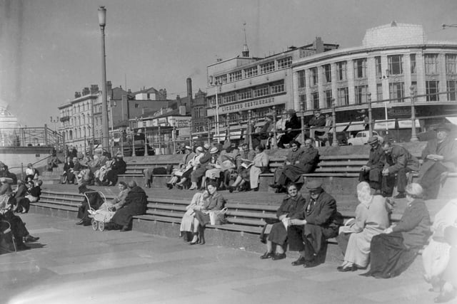Locals and visitors enjoying a spell of sunshine on the Promenade close to Church Street, Blackpool in 1959. Landmarks in the backgrund include The Clifton Hotel, Robert's Oyster Rooms The Savoy Cafe complex and Burtons menswear shop