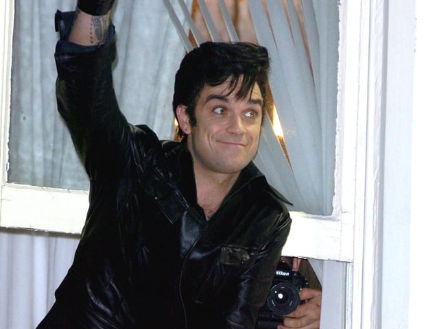Robbie Williams leaning out of a window at the Belle Vue Hotel in Whitegate Drive, waving to fans in the street below in 2005