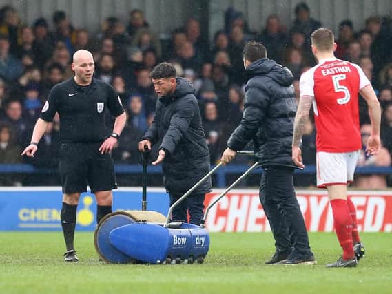 Fleetwood Town's Ash Eastham and referee Charles Breakspear watch on as the groundstaff tackle the pitch