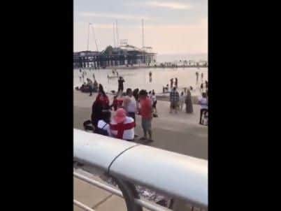 A screengrab from the video shows a woman enjoying the seaside with a St George's flag wrapped around her.