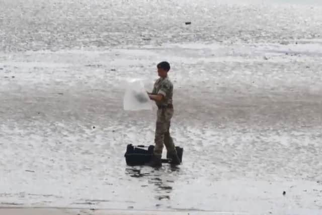 A military bomb disposal expert examines the object using a hand-held device.