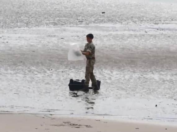 A military bomb disposal expert examines the object using a hand-held device.