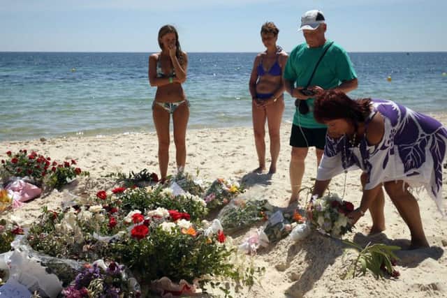 Tourists look at flowers that have been laid on the beach near the RIU Imperial Marhaba hotel in Sousse, Tunisia