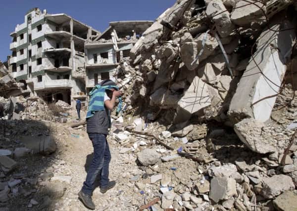 A Syrian covers his face as he walks with a friend between destroyed buildings in the old city of Homs, Syria,