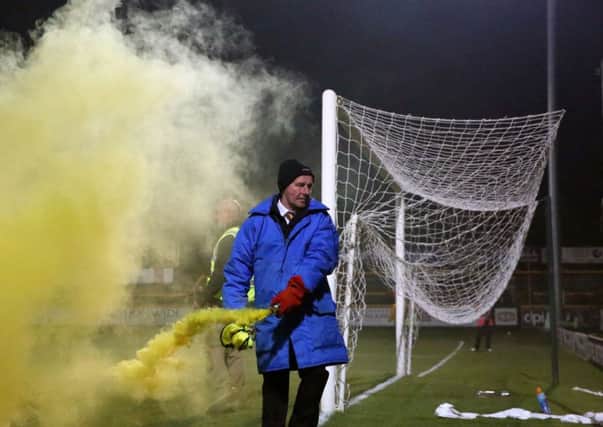 A steward carries a flare that was thrown onto the pitch during the Emirates FA Cup, First Round match at the Merseyrail Community Stadium