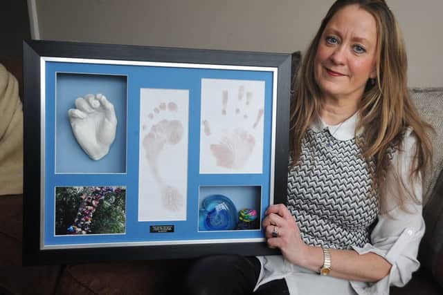 Joanne with a memory board of plaster casts and handprints of James.
