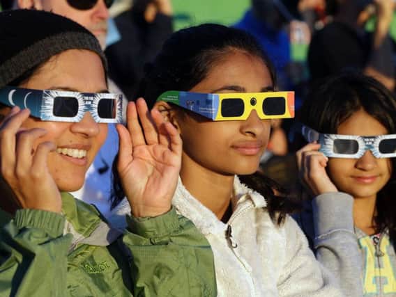 Schweta Kulkarni, from left, Rhea Kulkarni and Saanvi Kulkarni, from Seattle, try out their eclipse glasses on the sun at a gathering of eclipse viewers in Salem