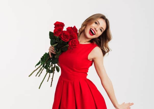 Full length portrait of a lovely young woman dressed in red dress holding bouquet of roses while standing and looking at camera isolated over white background